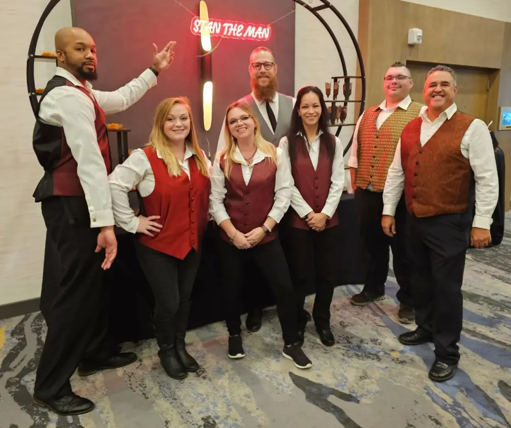 Seven casino-party dealers in coordinated vests pose together at an indoor event.